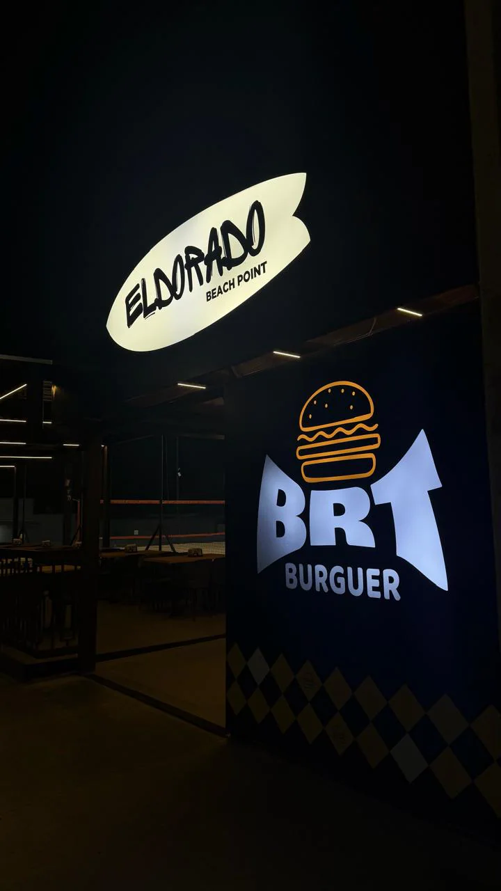 Fachada do BRT Burguer à noite, com o letreiro luminoso da marca e, acima, o letreiro do Eldorado Beach Point